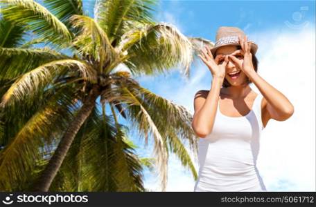 summer holidays, travel, people and vacation concept - happy young woman in hat making finger glasses over exotic tropical beach with palm tree background. happy young woman in hat on summer beach