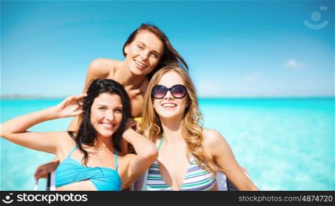 summer holidays, travel, people and vacation concept - happy young women in bikinis and shades over sea beach background