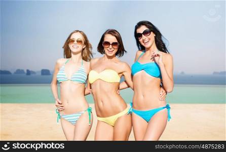 summer holidays, travel, people and vacation concept - happy young women in bikinis and shades over infinity edge pool background