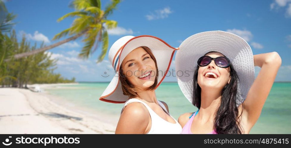 summer holidays, travel, people and vacation concept - happy young women in hats over exotic tropical beach with palm trees and sea shore background