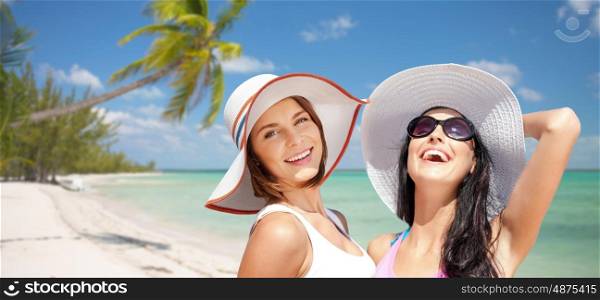summer holidays, travel, people and vacation concept - happy young women in hats over exotic tropical beach with palm trees and sea shore background