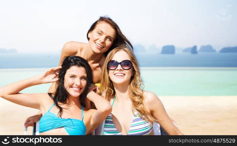 summer holidays, travel, people and vacation concept - happy young women in bikinis and shades over infinity edge pool background