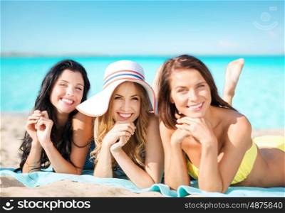 summer holidays, travel, people and vacation concept - happy young women in bikinis sunbathing over exotic tropical beach background