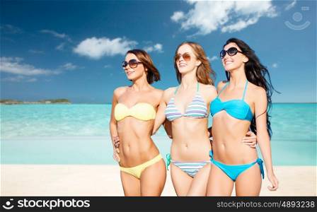 summer holidays, travel, people and vacation concept - happy young women in bikinis and shades over exotic tropical beach background