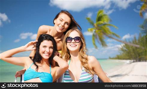 summer holidays, travel, people and vacation concept - happy young women in bikinis and shades over exotic tropical beach with palm trees and sea shore background