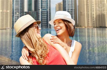 summer holidays, travel, people and vacation concept - happy young women in hats over infinity edge pool in dubai background