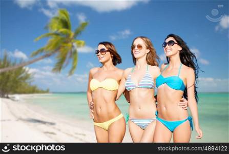 summer holidays, travel, people and vacation concept - happy young women in bikinis and shades over exotic tropical beach with palm trees and sea shore background