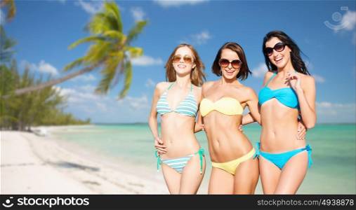 summer holidays, travel, people and vacation concept - happy young women in bikinis and shades over exotic tropical beach with palm trees and sea shore background. happy young women in bikinis on summer beach