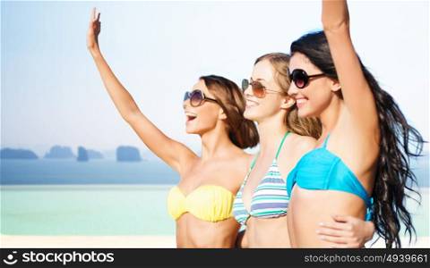 summer holidays, travel, people and vacation concept - happy young women in bikinis and shades hugging and waving hands over sea and infinity edge pool background. happy young women in bikinis on summer beach