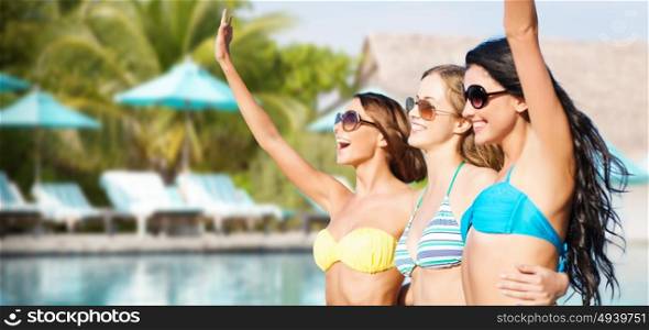 summer holidays, travel, people and vacation concept - happy young women in bikinis and shades hugging and waving hands over swimming pool background. happy young women in bikinis on summer beach