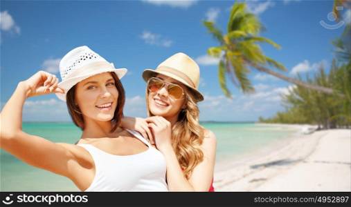 summer holidays, travel, people and vacation concept - happy young women in hats over exotic tropical beach with palm trees and sea shore background. happy young women in hats on summer beach