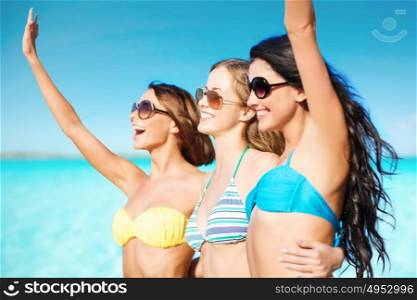summer holidays, travel, people and vacation concept - happy young women in bikinis and shades hugging and waving hands on beach over sea and blue sky background. happy young women in bikinis on summer beach