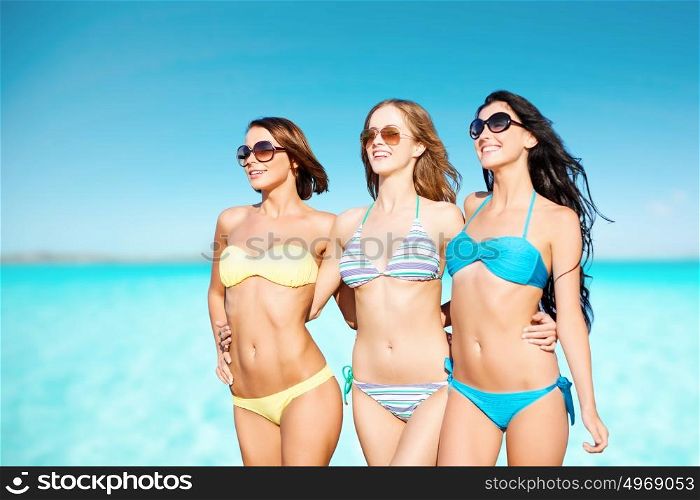 summer holidays, travel, people and vacation concept - happy young women in bikinis and shades over blue sky and sea background. happy young women in bikinis over blue sky and sea