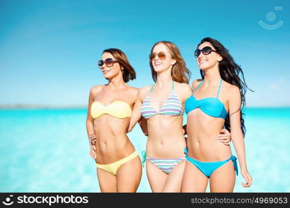 summer holidays, travel, people and vacation concept - happy young women in bikinis and shades over blue sky and sea background. happy young women in bikinis over blue sky and sea