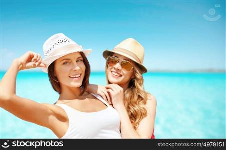 summer holidays, travel, people and vacation concept - happy young women in hats over sea beach background. happy young women in hats on summer beach