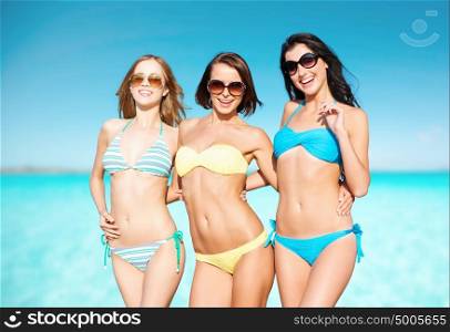 summer holidays, travel, people and vacation concept - happy young women in bikinis and shades over sea beach background. happy young women in bikinis on summer beach