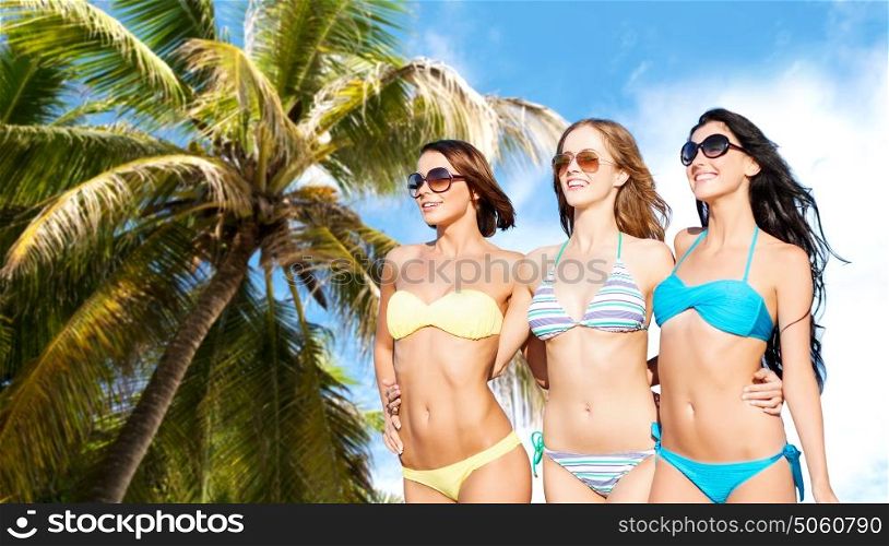 summer holidays, travel, people and vacation concept - happy young women in bikinis and shades over exotic tropical beach with palm tree background. happy young women in bikinis on summer beach