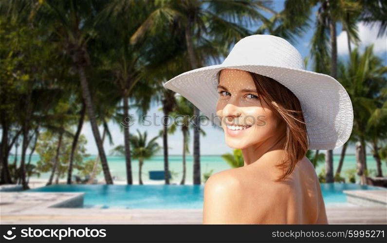 summer holidays, travel, people, tourism and vacation concept - happy young woman in sunhat on beach over swimming pool and palm trees at hotel resort background