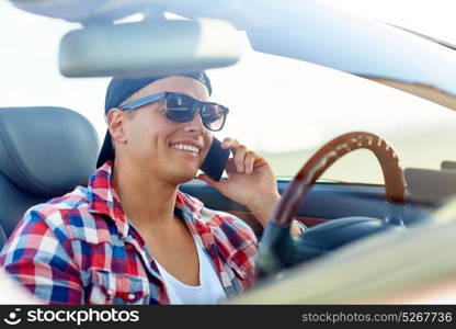 summer holidays, travel, road trip and people concept - happy smiling young man calling on smartphone while driving convertible car. young man driving car and calling on smartphone