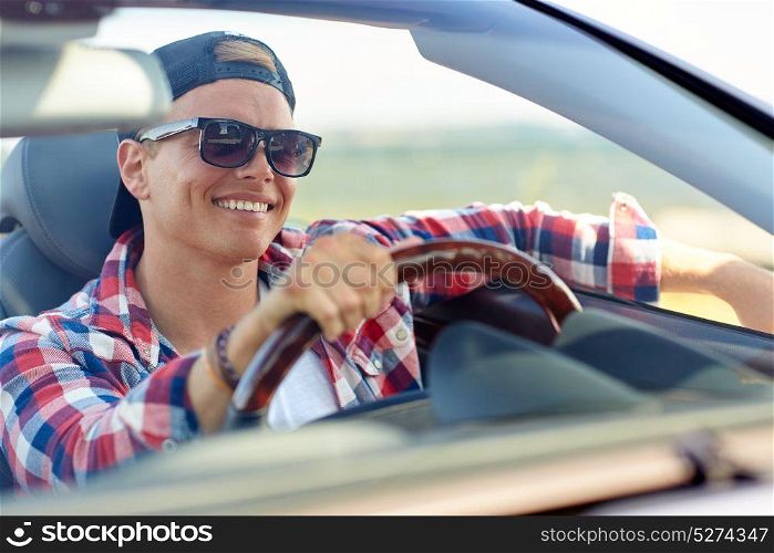 summer holidays, travel, road trip and people concept - happy smiling young man in sunglasses and cap driving convertible car. happy young man in shades driving convertible car
