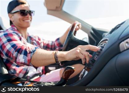 summer holidays, travel, road trip and people concept - happy young man driving convertible car and pushing button on dashboard. happy young man driving convertible car