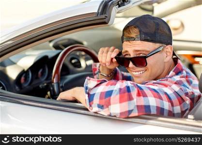 summer holidays, travel, road trip and people concept - smiling handsome young man in sunglasses and cap driving convertible car. happy young man in shades driving convertible car