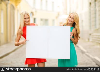 summer holidays, , travel, tourism and advertisement concept - two happy blonde women with blank white board in the city