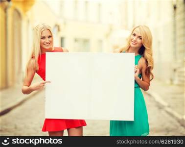 summer holidays, , travel, tourism and advertisement concept - two happy blonde women with blank white board in the city
