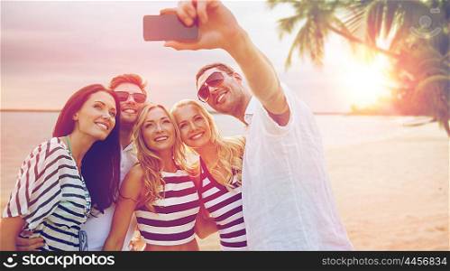 summer holidays, travel, tourism, technology and people concept - group of smiling friends with smartphone photographing and taking selfie over exotic tropical beach background