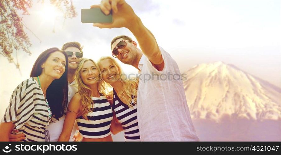 summer holidays, travel, tourism, technology and people concept - group of smiling friends with smartphone photographing and taking selfie over fujiyama mountain in japan background