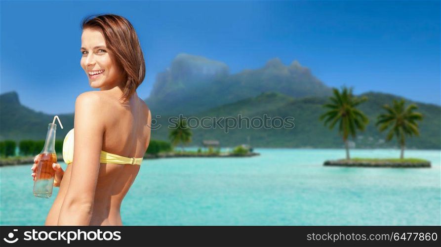 summer holidays, vacation and beach concept - smiling woman in bikini with bottle of non alcoholic drink over bora bora island beach background. woman in bikini with drink on bora bora beach. woman in bikini with drink on bora bora beach