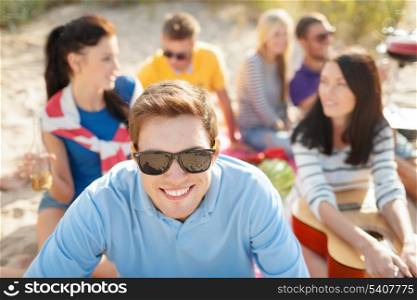 summer, holidays, vacation and happiness concept - smiling man in sunglasses having fun on the beach with company on the back