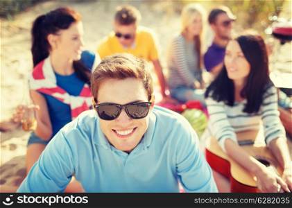 summer, holidays, vacation and happiness concept - smiling man in sunglasses having fun on the beach with company on the back