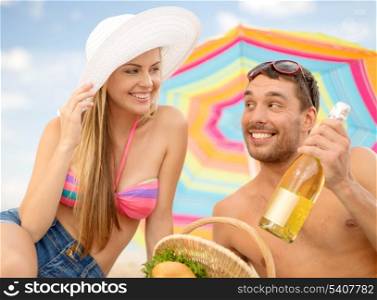 summer, holidays, vacation and happy people concept - smiling couple having picnic on the beach under colorful umbrella