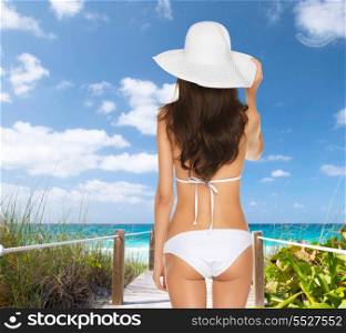 summer holidays, vacation and lingerie concept - back view of beautiful woman in white bikini and hat on a beach