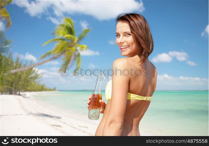 summer holidays, vacation and people concept - happy smiling young woman in bikini with bottle of drink over exotic tropical beach with palm trees background