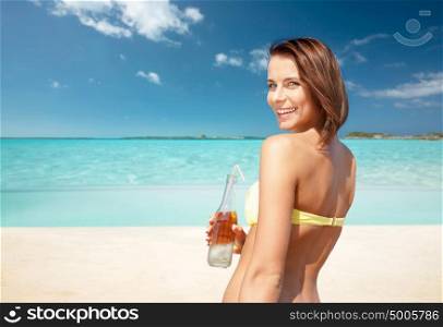 summer holidays, vacation and people concept - happy smiling young woman in bikini with bottle of drink over exotic tropical beach background. woman in bikini with bottle of drink on beach