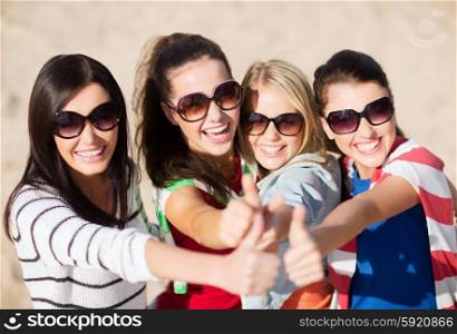 summer holidays, vacation and people concept - happy teenage girls in sunglasses or young women showing thumbs up on beach