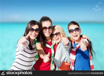 summer holidays, vacation and people concept - happy teenage girls in sunglasses or young women showing thumbs up over beach background