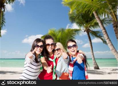 summer holidays, vacation and people concept - happy teenage girls in sunglasses or young women showing thumbs up over tropical beach background