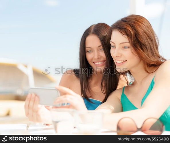 summer holidays, vacation and technology concept - girls looking at smartphone in cafe on the beach