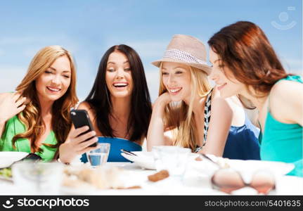 summer holidays, vacation and technology - girls looking at smartphone in cafe on the beach