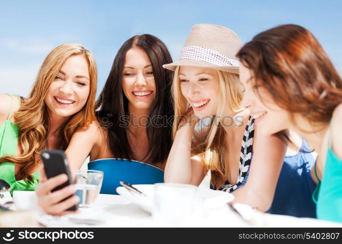 summer holidays, vacation and technology - girls looking at smartphone in cafe on the beach