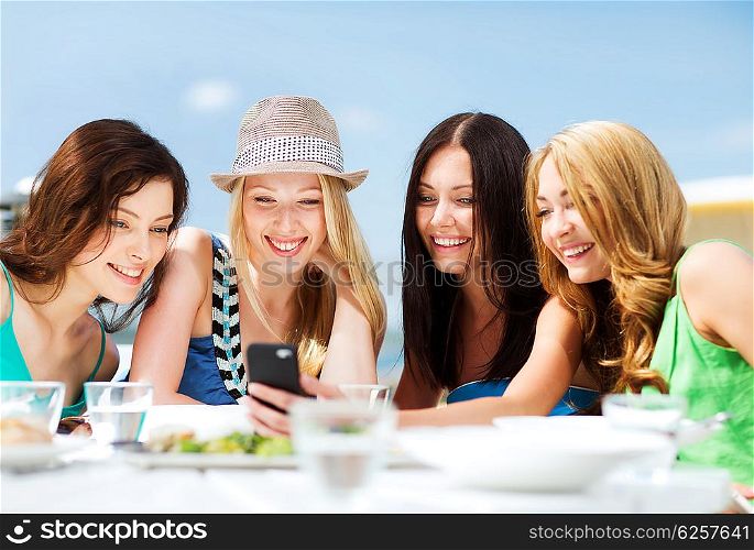 summer holidays, vacation and technology - girls looking at smartphone in cafe on the beach