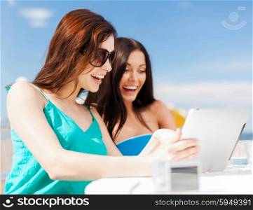 summer holidays, vacation and technology - girls looking at tablet pc in cafe on the beach