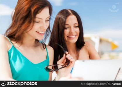 summer holidays, vacation and technology - girls looking at tablet pc in cafe on the beach