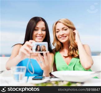 summer holidays, vacation and technology - girls taking photo with digital camera in cafe on the beach