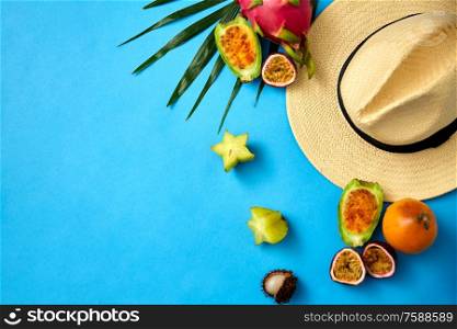 summer holidays, vacation and travel concept - close up of straw hat and exotic fruits on blue background. straw hat and exotic fruits on blue background