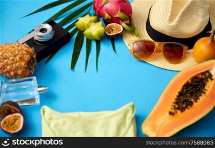 summer holidays, vacation and travel concept - close up of sunglasses, straw hat, camera and exotic fruits with palm leaf and clothes on blue background. sunglasses, hat, camera, fruits and clothes