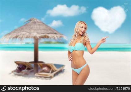 summer holidays, vacation and travel concept - happy smiling young woman in bikini swimsuit pointing finger over tropical beach of maldives background. happy smiling young woman in bikini on beach